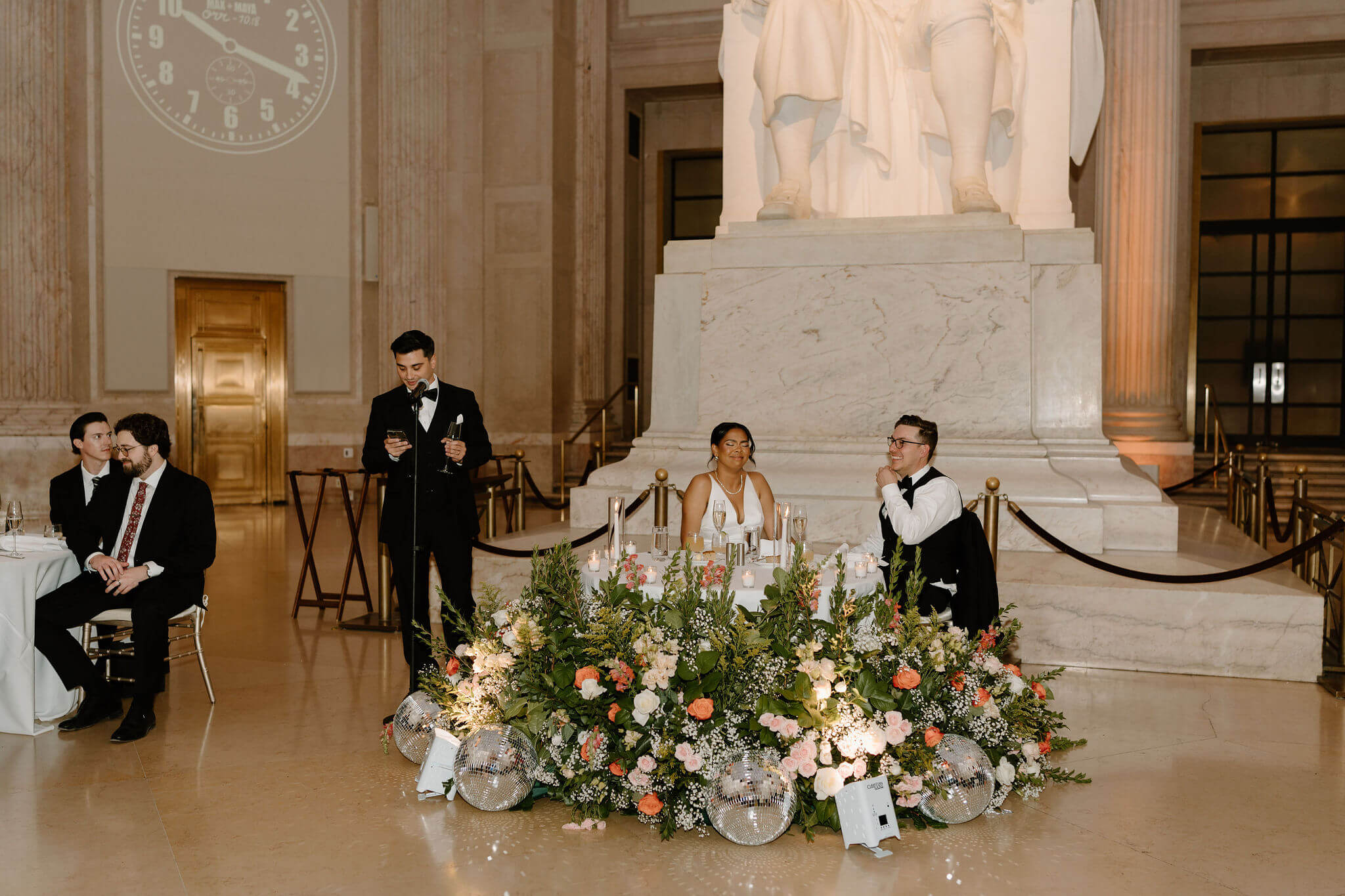 one best man giving a speech during a wedding reception, standing next to the sweetheart table