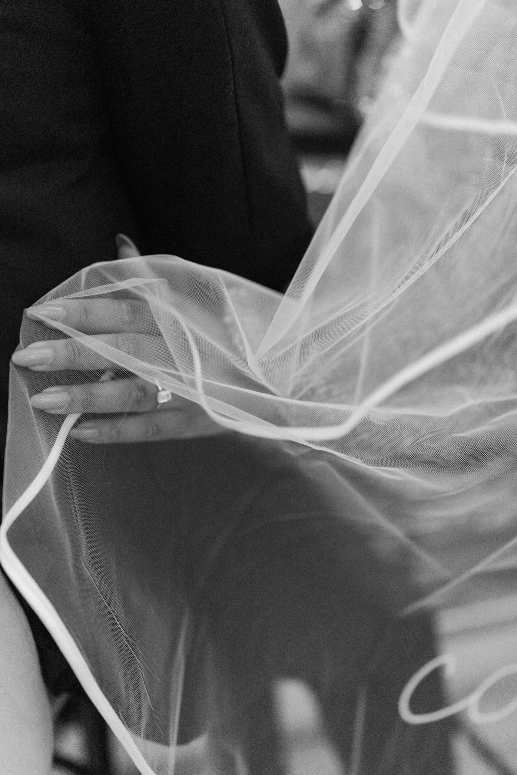 close up of emerald cut engagement ring on bride's hand, as she holds the tulle of her veil