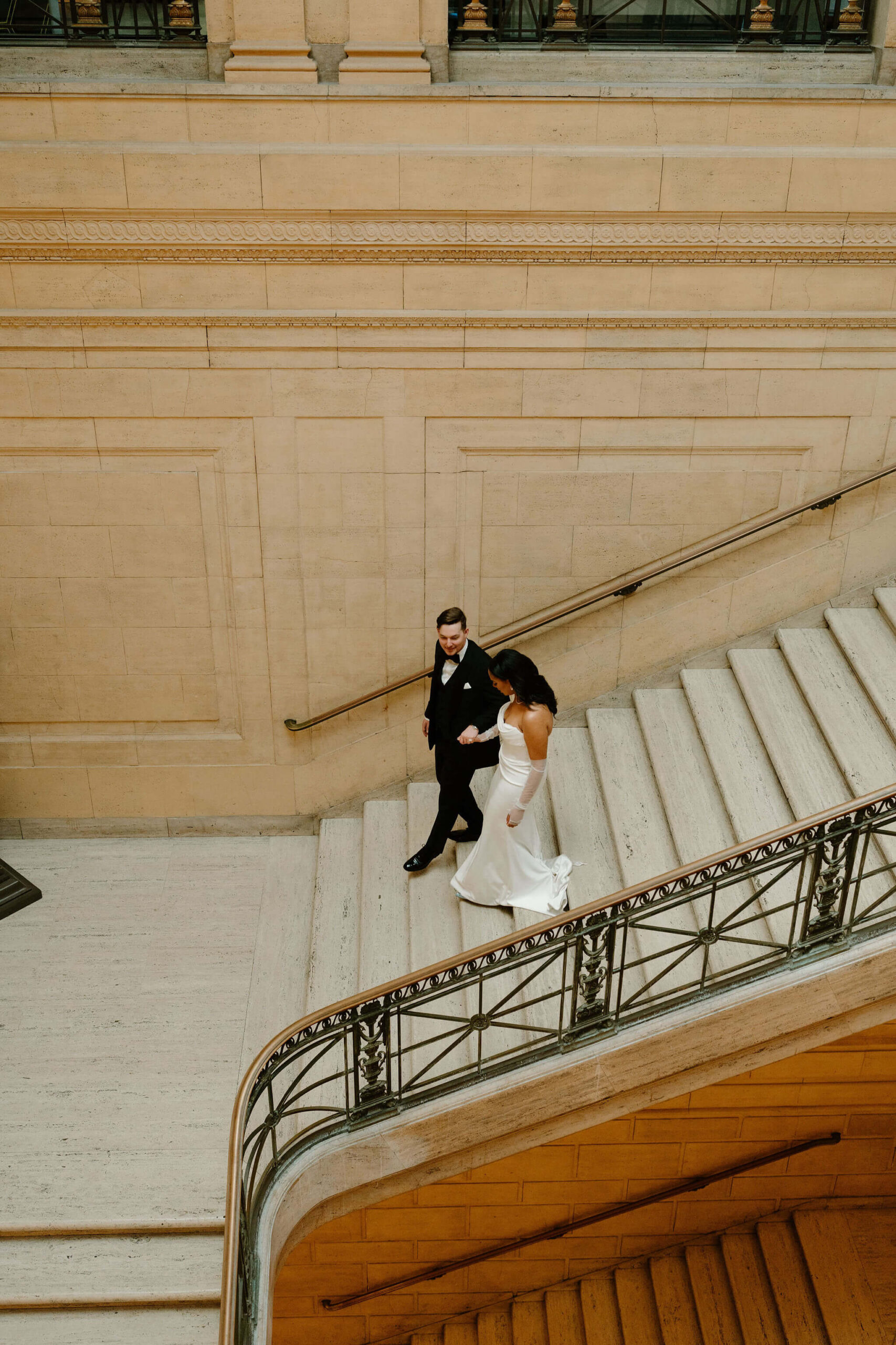 aerial image of a groom leading his bride down a large marble staircase at the Franklin Institute on their wedding day