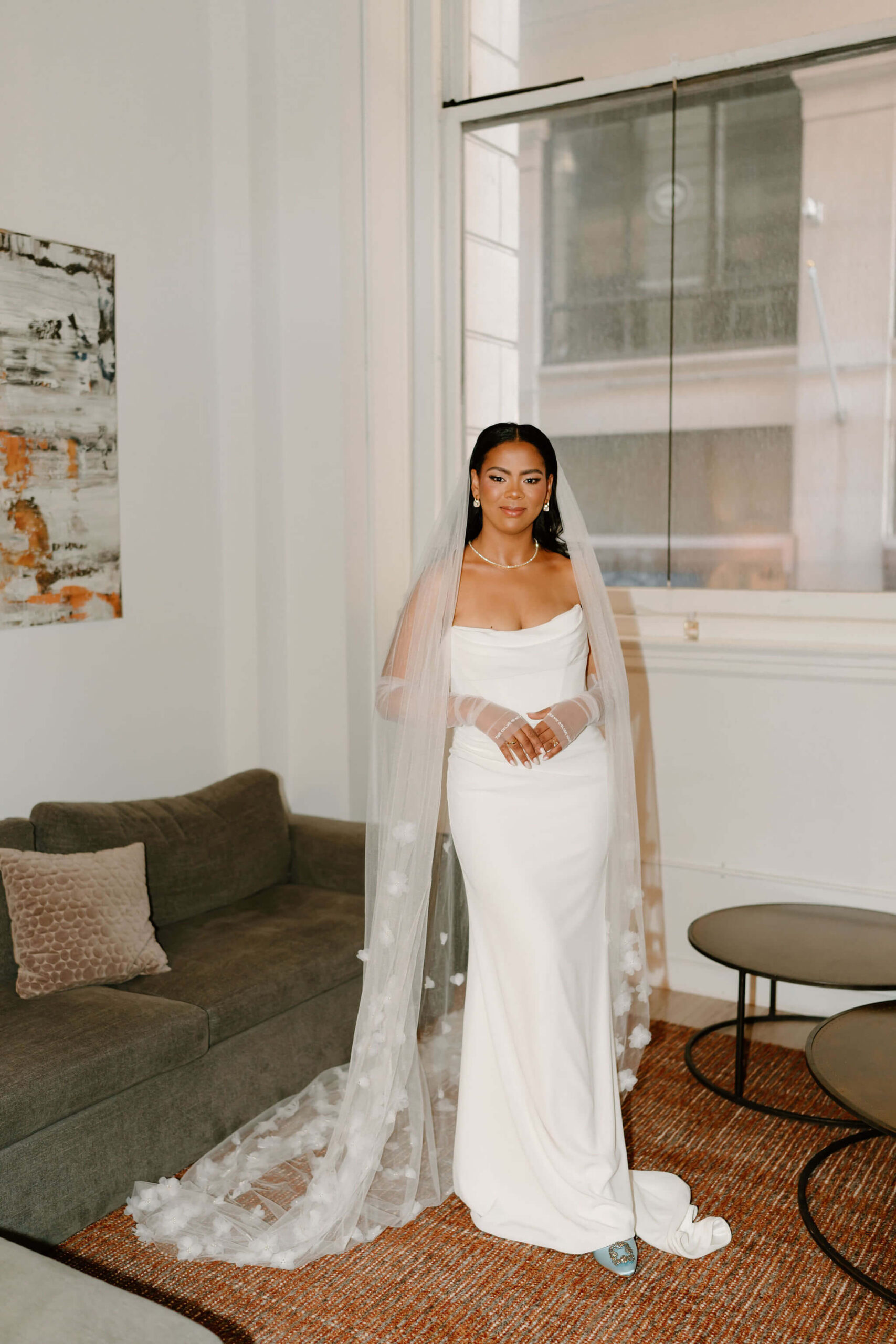 bride wearing a long wedding gown, a cathedral-length veil, blue heels, and fingerless tulle gloves, gently holding her hands in front of her and smiling softly at the camera