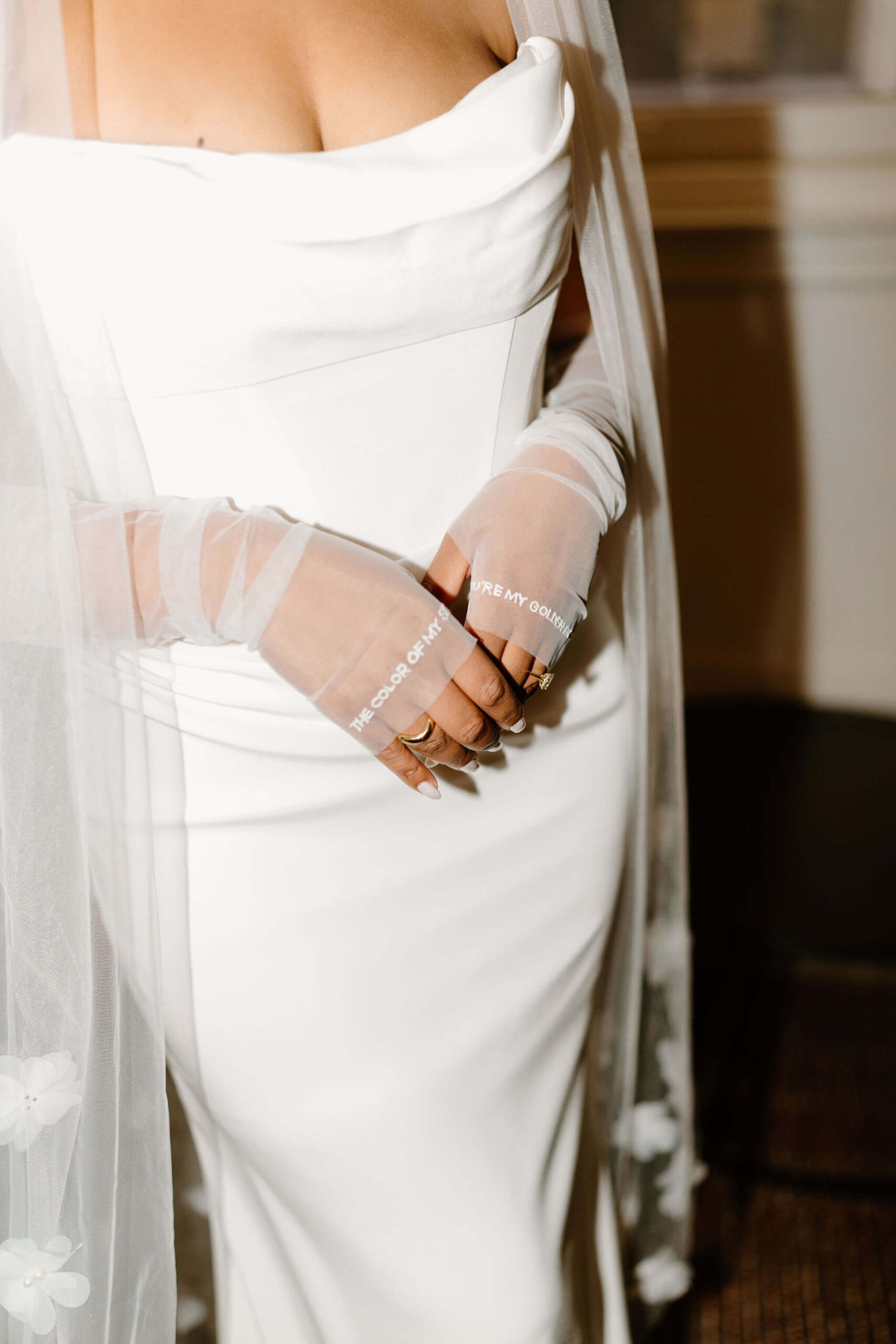 close up of bride's hands crossed gently in front of her, wearing fingerless gloves that read "you're my golden hour / the color of my sky"