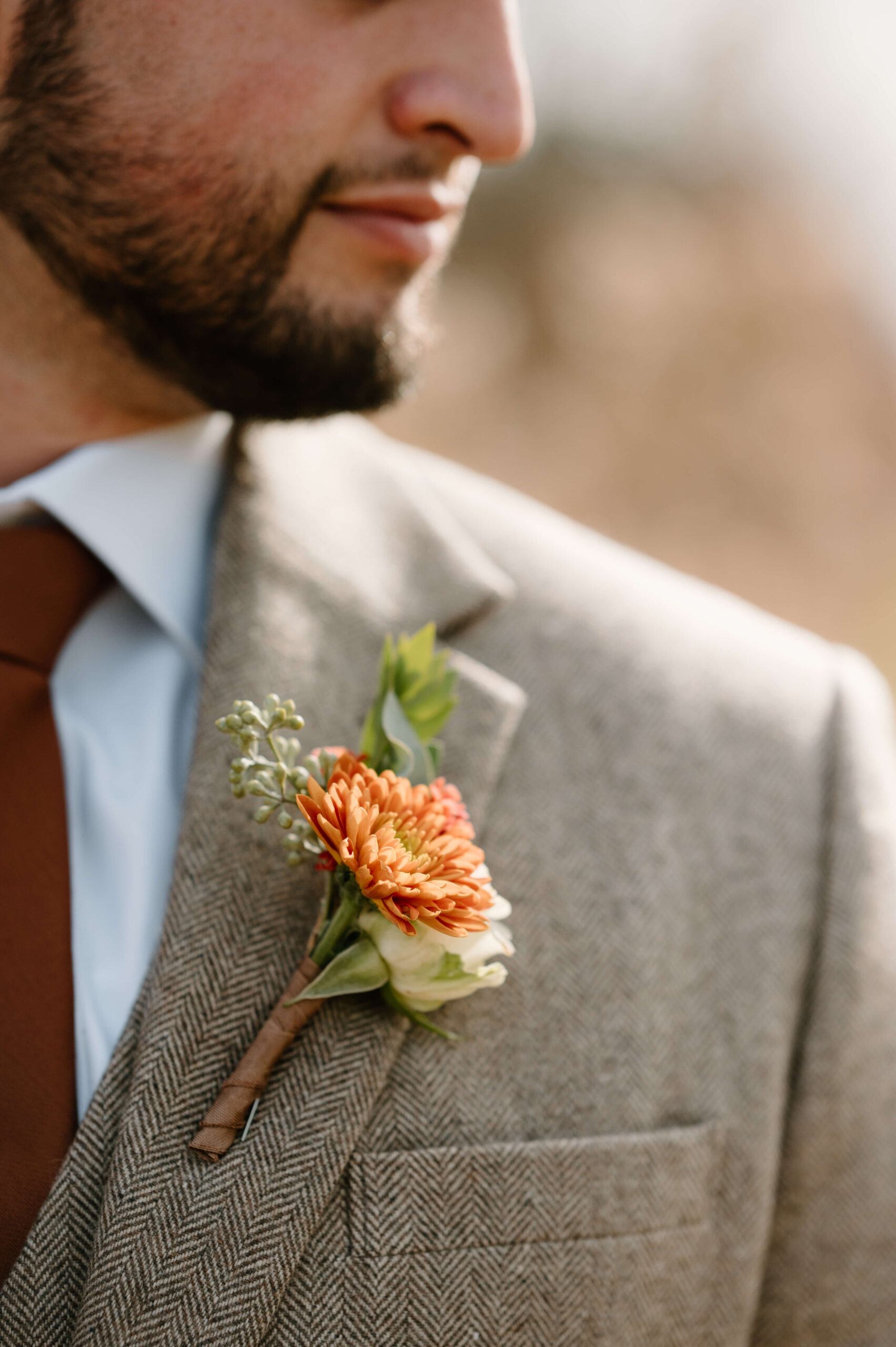 close up of groom's orange floral boutonniere against his tweed suit, with groom's face in profile looking off-camera