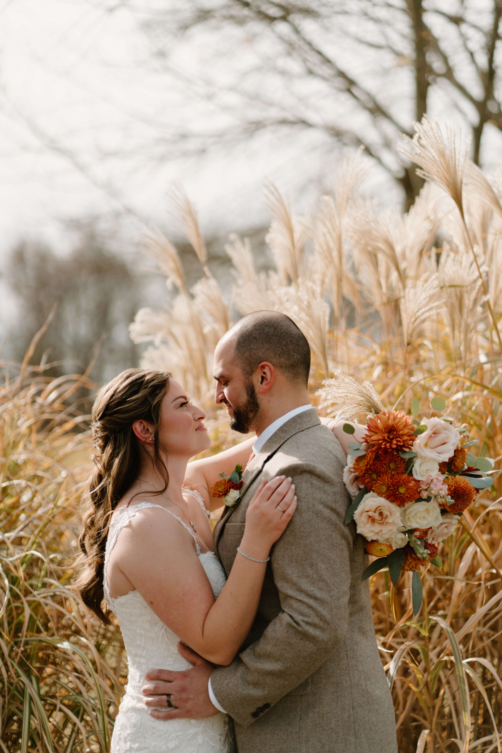 close-up of bride and groom embracing on their wedding day in front of a large patch of pampas grass