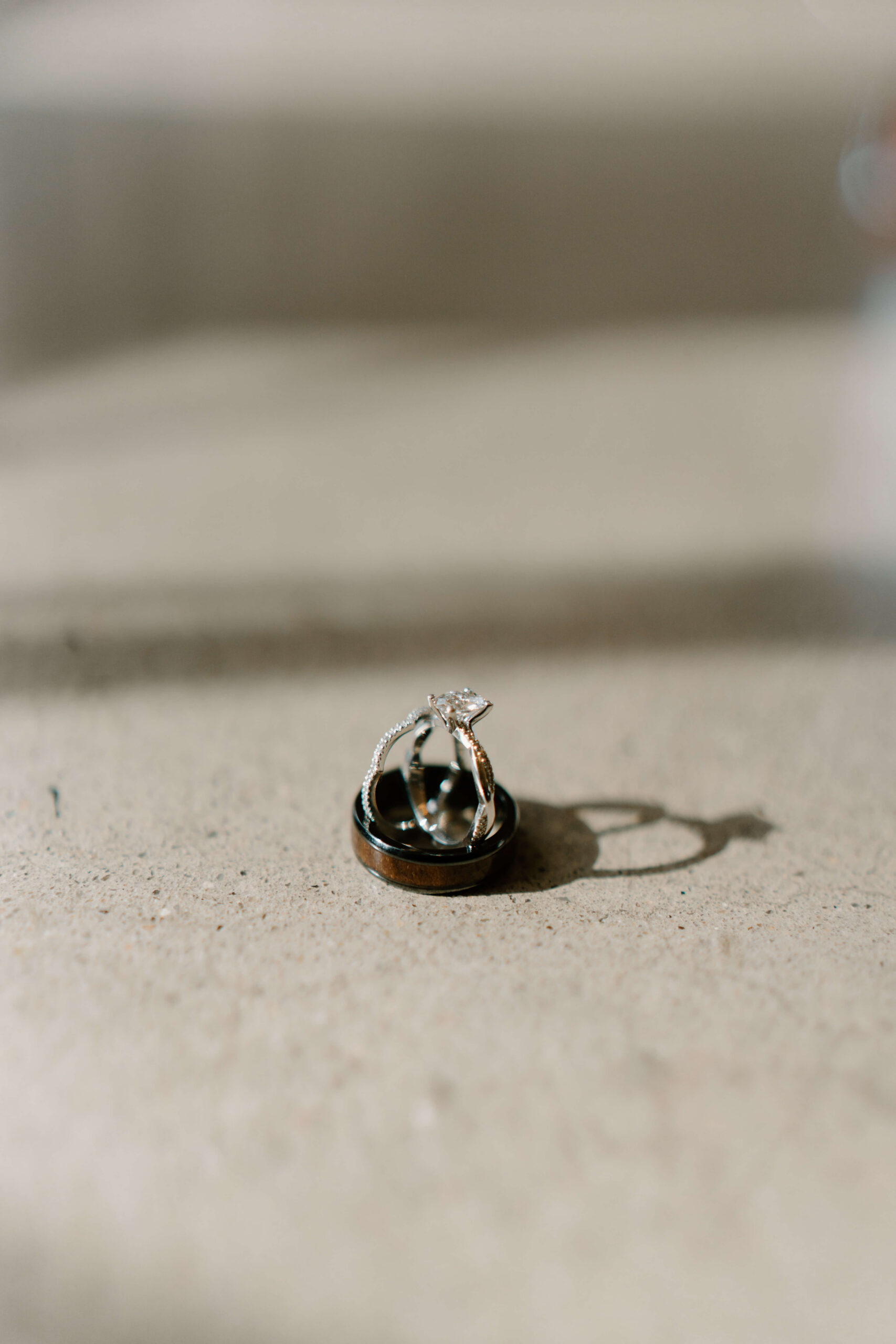 bride's engagement ring and wedding band propped up inside groom's wedding band, casting an interesting shadow on the surface next to it
