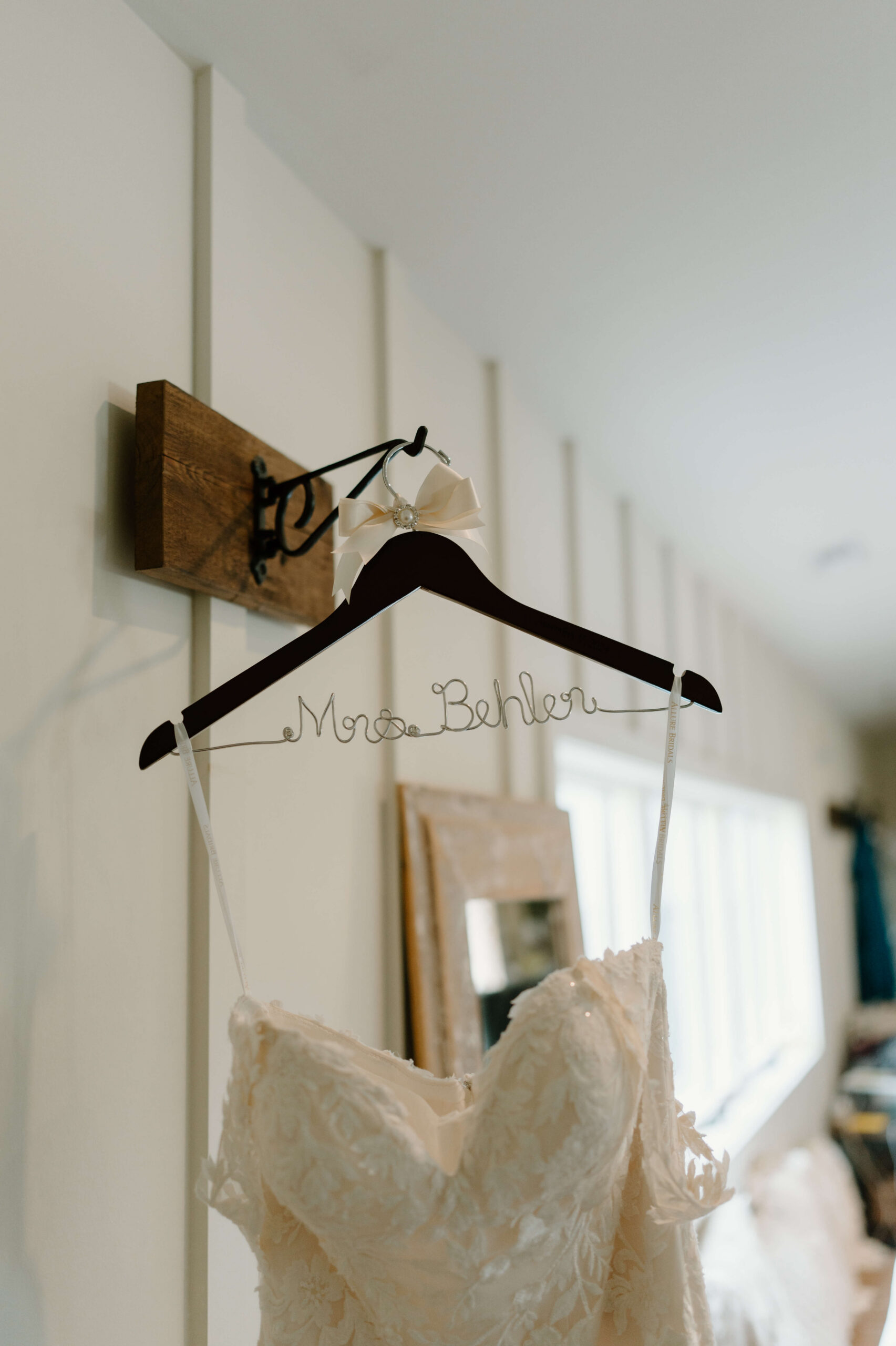 custom wooden hanger with metal shaped to read "Mrs. Behler", with a wedding dress hanging on it