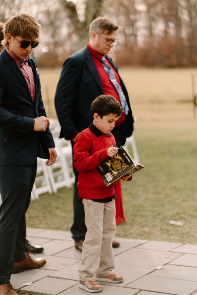 a young boy standing and reading a book during cocktail hour at a wedding