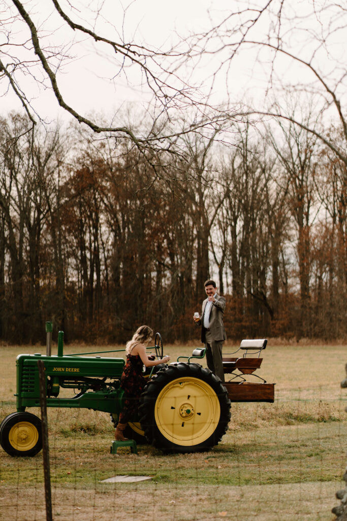 two guests climbing on an antique green John Deere tractor during cocktail hour
