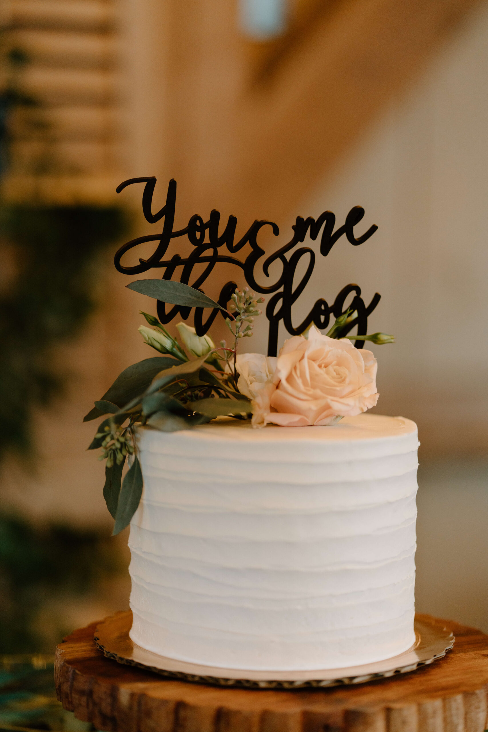 small wedding cake decorated with flowers and a sign reading "You & Me & the Dog"