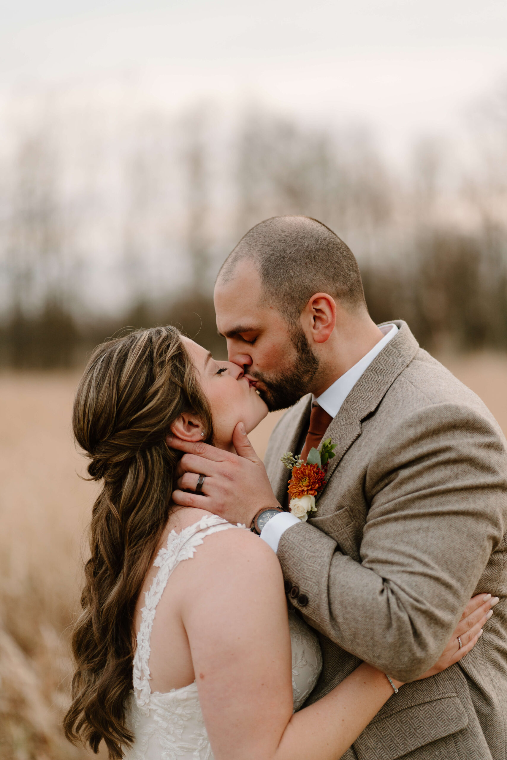 close up image of groom holding bride's face and kissing her in a wide open field