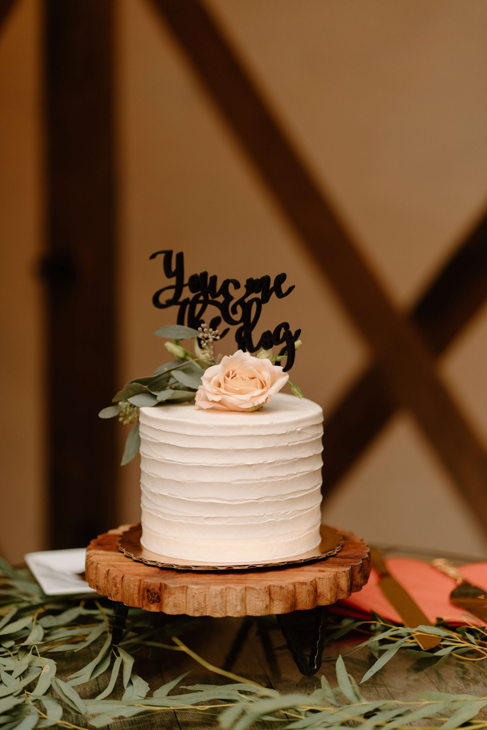 small wedding cake decorated with flowers and a sign reading "You & Me & the Dog"