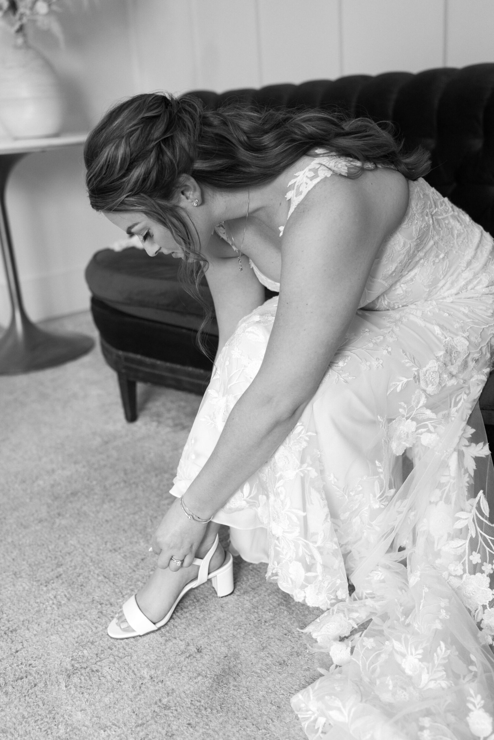black and white image of bride seated, putting on her heels