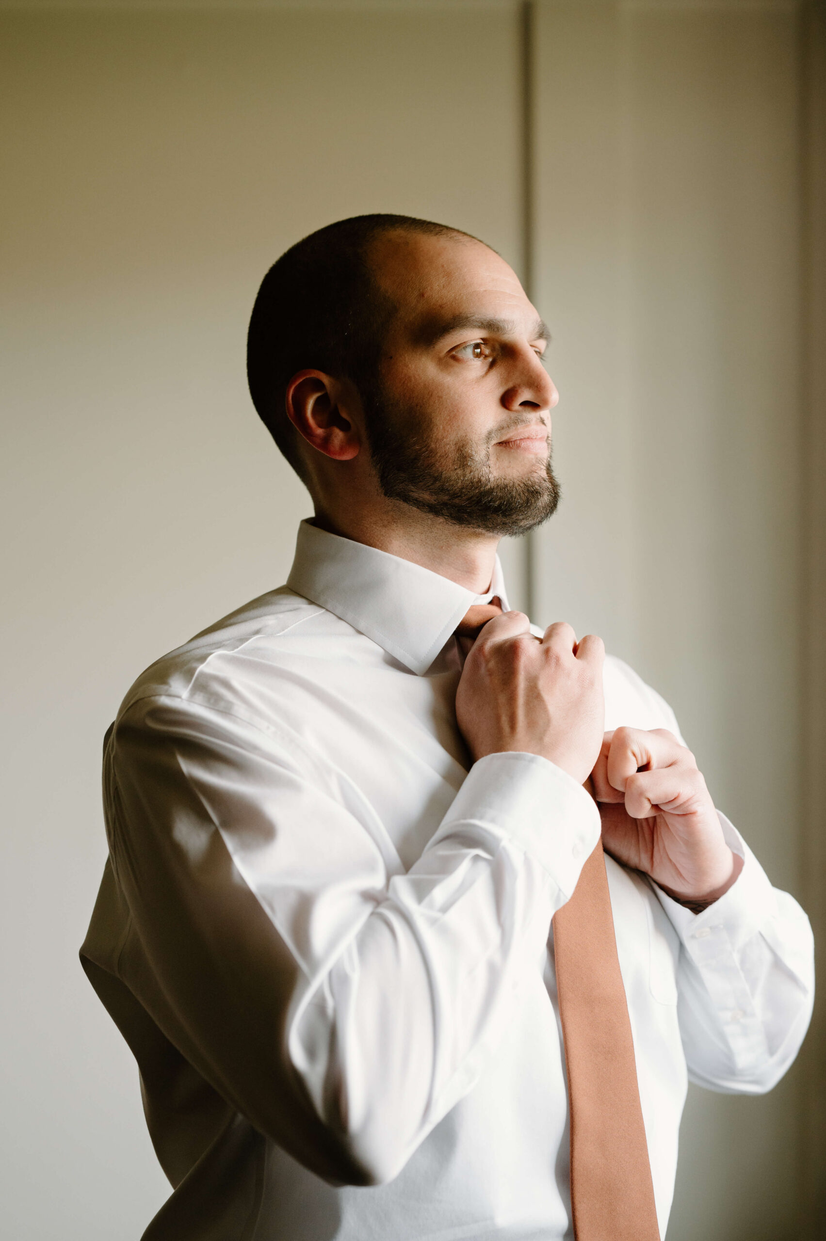 groom looking off-camera, straightening his brown tie